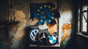 Volkswagen už nečaká jednoduchá vnútorná reštrukturalizácia. Nemecká skupina zvažuje plán redukcie, ktorý by mohol ovplyvniť až 100 000 pracovných miest na celom svete a viesť k zatvoreniu štyroch závodov v Nemecku – Hannoveri, Zwickau, Emdene a Neckarsulme (posledný z nich je spojený s Audi) po predchádzajúcej dohode s odbormi o zrušení 50 000 pracovných miest do roku 2030. Tento údaj stavia najväčšiu nemeckú priemyselnú spoločnosť do stredu svojej najvážnejšej pracovnej krízy za posledné desaťročia. Problémom nie je len Volkswagen. BMW vyčlenilo až 1 miliardu EUR na náklady na reštrukturalizáciu, čo je podľa analytikov až o 10 000 menej pracovných miest a 15 % zníženie jej európskej výroby. Mercedes-Benz, zasiahnutý klesajúcimi maržami, už v Nemecku zaznamenal približne 5 500 dobrovoľných odchodov a tlačí na znižovanie interných nákladov so zameraním na bonusy a pracovné podmienky. Srdcom úpravy je Nemecko, ale dosah je európsky. Nemecký automobilový priemysel stále podporuje približne 700 000 priamych pracovných miest, hoci čísla zamestnanosti klesli na najnižšiu úroveň od roku 2011. Roky model fungoval na jasnom vzorci: spaľovacie motory s vysokou maržou, masívny export a Čína ako stroj na zisk. Táto éra sa skončila – pretože študent prekonal učiteľa. Čína už len nekupuje nemecké autá. Vytvára ich, vylepšuje a exportuje. Značky ako BYD, Chery, SAIC, Leapmotor a Xiaomi získali v Európe podiel na trhu s lacnejšími, dobre vybavenými elektrickými a hybridnými vozidlami, za ktorými stojí rozhodujúca priemyselná výhoda: kontrola nad batériami, kritickými materiálmi, rozsahom a štátnou podporou. V Číne klesol trhový podiel zahraničných výrobcov z približne 57 % v roku 2020 na 32 % v roku 2025. Volkswagen stratil dominantné postavenie v prospech BYD, zatiaľ čo Porsche znížilo svoj export do krajiny z takmer 100 000 kusov v roku 2021 na približne 40 000 v roku 2025. To je prenosový reťazec problému: nižšie zisky v Číne, tlak na ceny v Európe, clá a rozdiely v Spojených štátoch, vysoké náklady na energiu v Nemecku a elektrický prechod, ktorý si vyžaduje masívne investície práve vtedy, keď marže klesajú. Jedna vec však musí byť úplne jasná: dokonalá búrka nespadla z neba. Bol vybudovaný v priebehu rokov samoľúbymi podnikovými rozhodnutiami a európskou politikou, ktorá urýchlila elektrifikáciu bez toho, aby si najprv zabezpečila technologickú suverenitu, domáce batérie alebo konkurencieschopnú energiu. Takmer všetci odborníci sa zhodujú, že išlo o samovraždu, pred ktorou všetci varovali. Volkswagen je najextrémnejší prípad, no nie je jediný. Bosch pripravuje okolo 18 500 rezov. Schaeffler a Aumovio tiež rušia pracovné miesta a rušia prevádzky. To potvrdzuje, že kríza ovplyvňuje nielen viditeľné značky, ale celý dodávateľský reťazec: komponenty, inžinierstvo, elektroniku, softvér, logistiku a subdodávateľov. Keď padne výrobca, padne s ním aj ekosystém. Francúzsko vidí rovnaký problém s Renaultom a Stellantisom. Renault stráca pôdu pod nohami proti čínskemu pokroku v oblasti elektrických vozidiel, zatiaľ čo Stellantis – Peugeot, Citroën, Opel, Fiat – má nadbytočnú kapacitu v niekoľkých európskych závodoch. Taliansko je vystavené prostredníctvom výrobných závodov Fiat a Stellantis. Španielsko, hoci je nákladovo konkurencieschopnejšie ako Nemecko, závisí od rozhodnutí prijatých inde: jeho továrne Stellantis, Volkswagen a Ford sú výrobné platformy, nie suverénne rozhodovacie centrá. V scenári nadmernej kapacity je tento rozdiel dôležitý. Ford ukazuje ďalší rozmer ústupu. Jej závod v Kolíne nad Rýnom prejde v roku 2026 na jednu smenu s tým súvisiacim znižovaním počtu pracovných miest. Nejde o ojedinelý prípad, ale o súčasť európskeho trhu, ktorý zostáva 16 % pod úrovňami pred pandémiou. Čínska konkurencia neprichádza na expandujúci kontinent, ale na slabý, regulovaný a drahý trh. Situácia je taká vážna, že dokonca aj Volkswagen ponúka možnosť čínskych partnerov vyrábať autá v málo využívaných európskych závodoch. Inými slovami, Európa by mohla skončiť prenájmom svojej nadbytočnej priemyselnej kapacity práve tým konkurentom, ktorí spustili reštrukturalizáciu. Kríza Volkswagenu nie je len nemecká, ani len automobilová. Je to varovanie pred cenou straty strategického odvetvia, zatiaľ čo sa chváli európskou autonómiou. Otázkou teraz nie je, koľko pracovných miest bude zrušených, ale kto bude kontrolovať továrne, technológiu a hodnotový reťazec, keď šok pominie. Strategická autonómia? Skôr absolútna závislosť vyrábaná v bruselských kanceláriách.